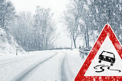 Snow covered road with a road sign showing the road is slippery