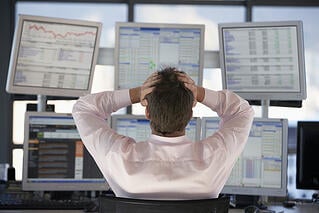 Picture of a man grasping his head looking at computer screens