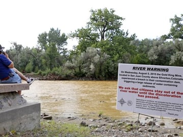 Person sitting next to a river with a river warning sign in the frame