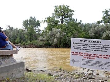 Person sitting next to a river with a river warning sign in the frame Person sitting next to a river with a river warning sign in the frame