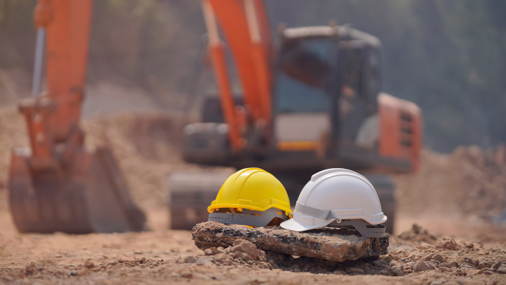 image of two construction hard hats in the foreground with an orange excavator behind