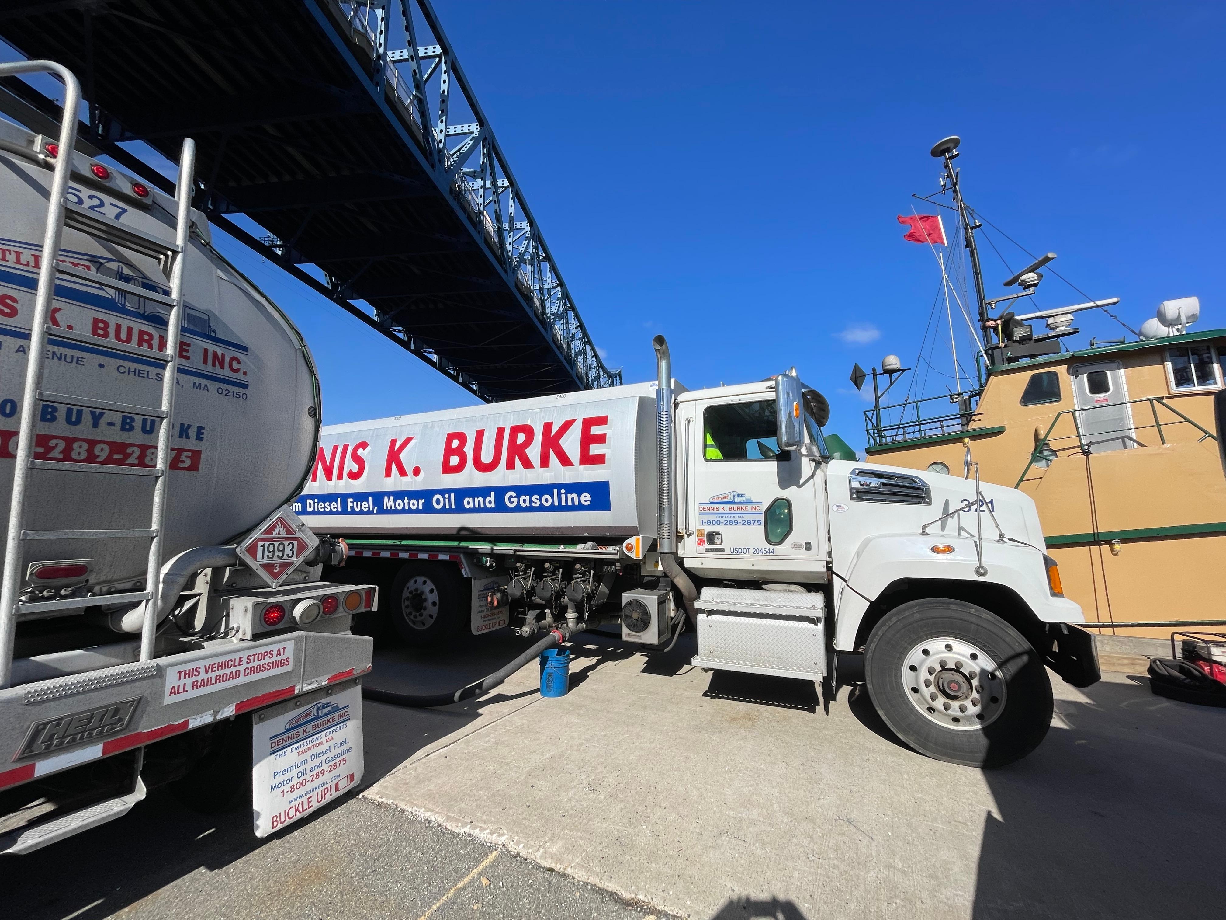 image of a dennis k burke oil truck under a bridge fueling a tug boat