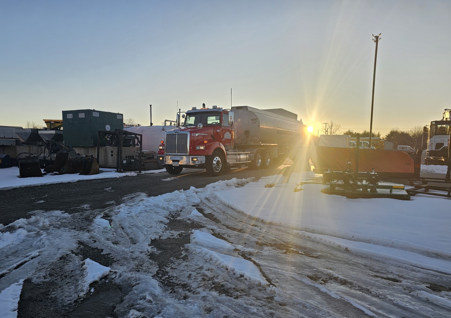 Sunset behind Dennis K Burke oil truck in snowy yard
